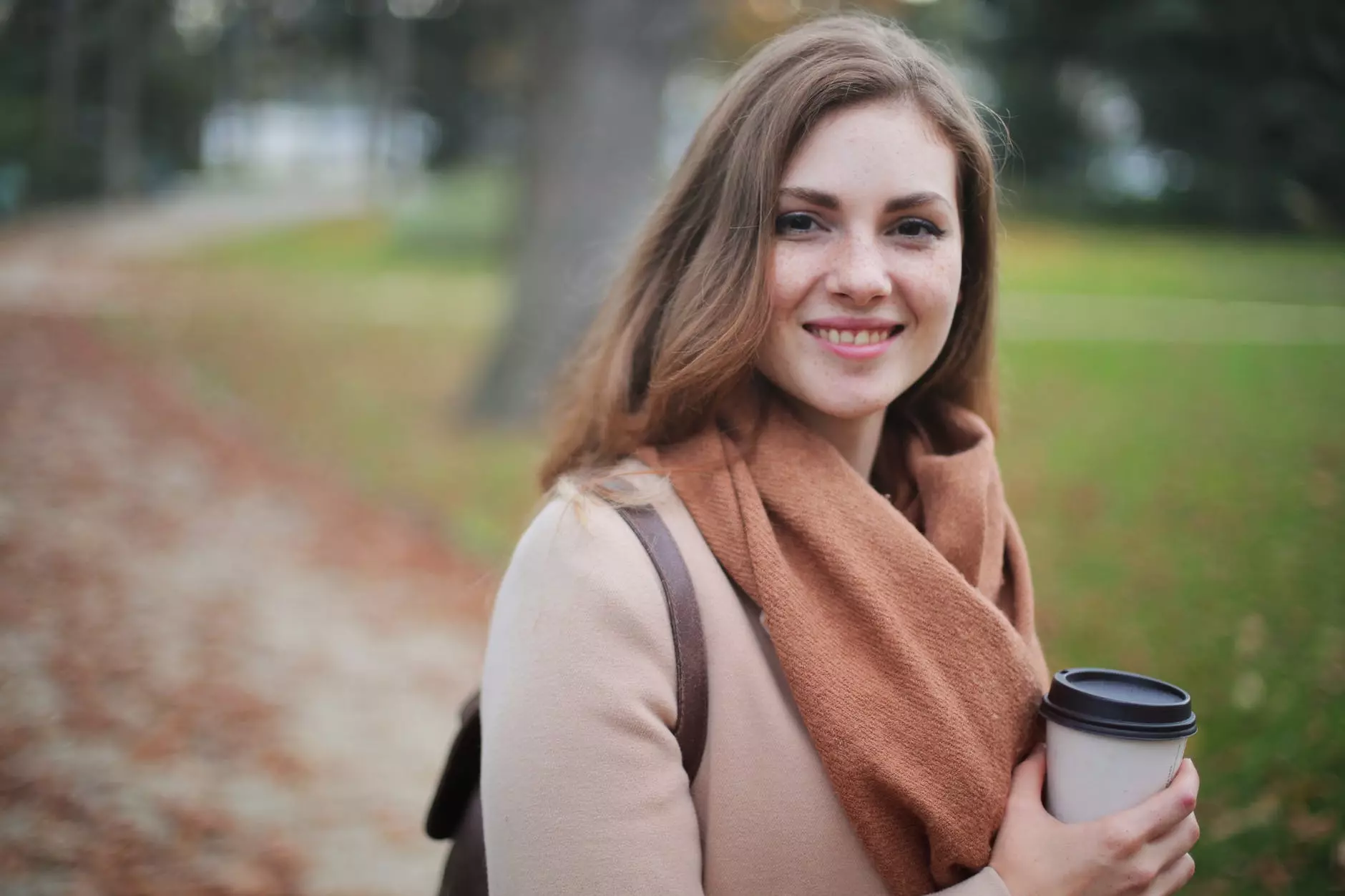 a girl in a beige coat holds a cup